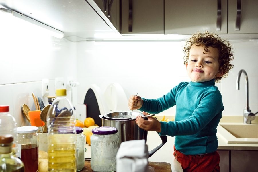 Curly-haired toddler enjoying fermentation cooking activities in modern kitchen with glass jars
