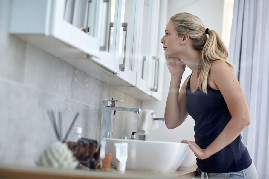 Woman applying ancient beauty rituals skincare routine in modern bathroom