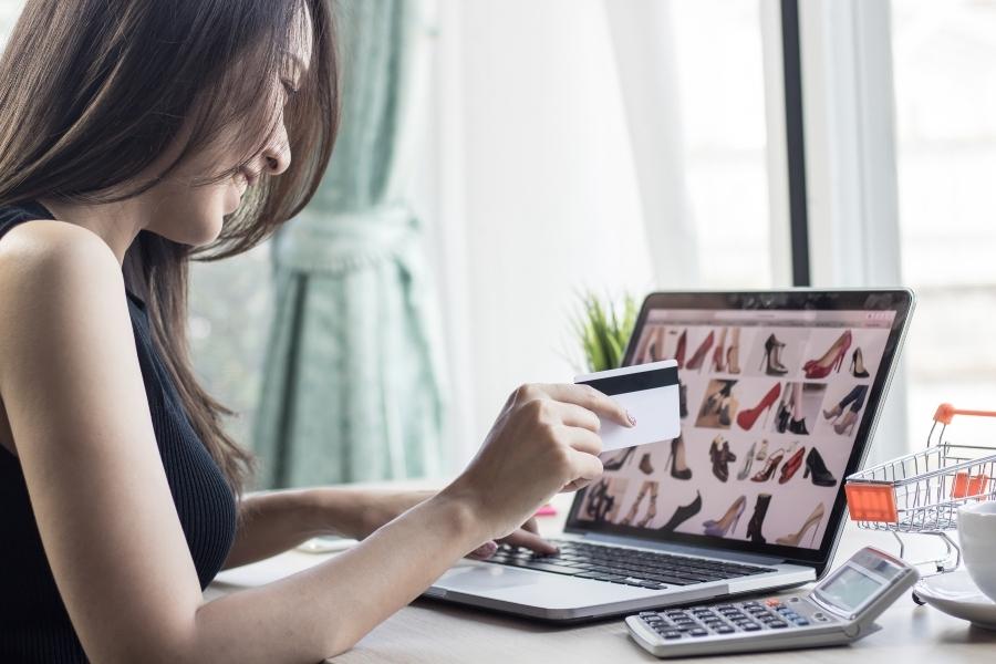 Woman doing online shopping for shoes on laptop with credit card and calculator