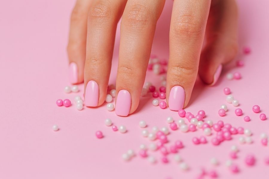 Pink press-on nails displayed artistically with decorative pearls showing professional finish