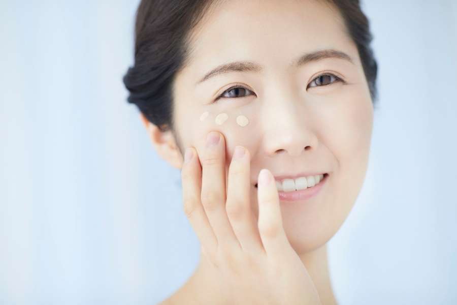 Smiling Asian woman learning how to apply foundation with fingertips on cheek