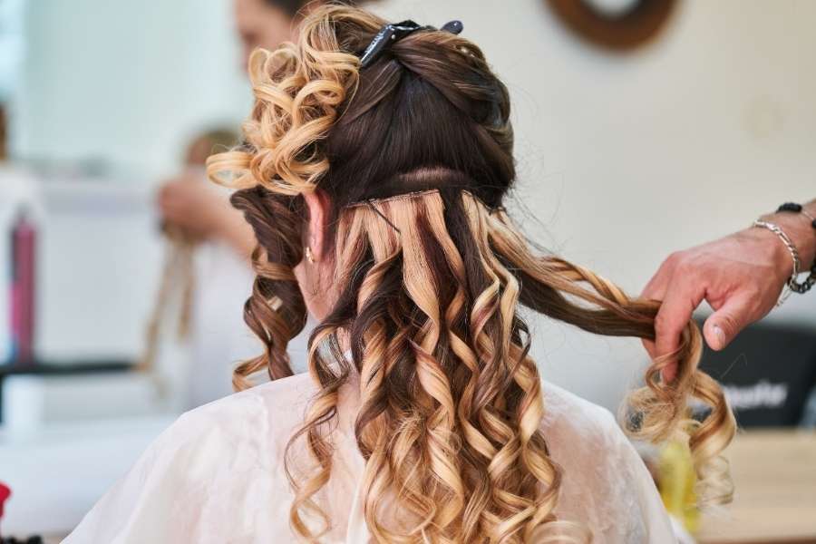 Professional stylist creating elegant Christmas party hairstyles with curling iron on blonde highlighted hair