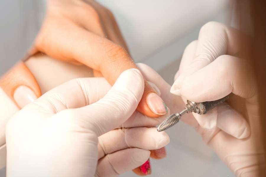 Nail technician performing professional gel polish removal using an electric nail file.