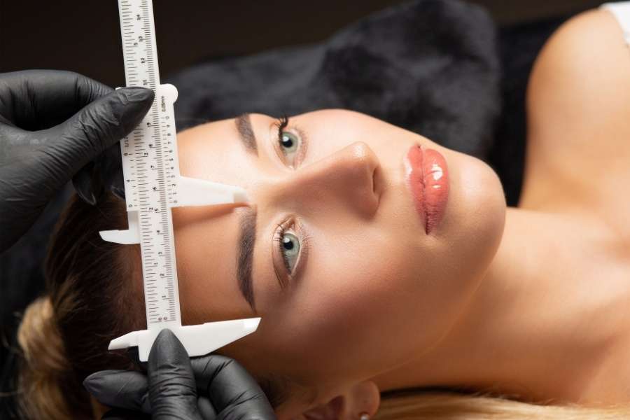 Professional eyebrow shaping consultation with precision measurement tools