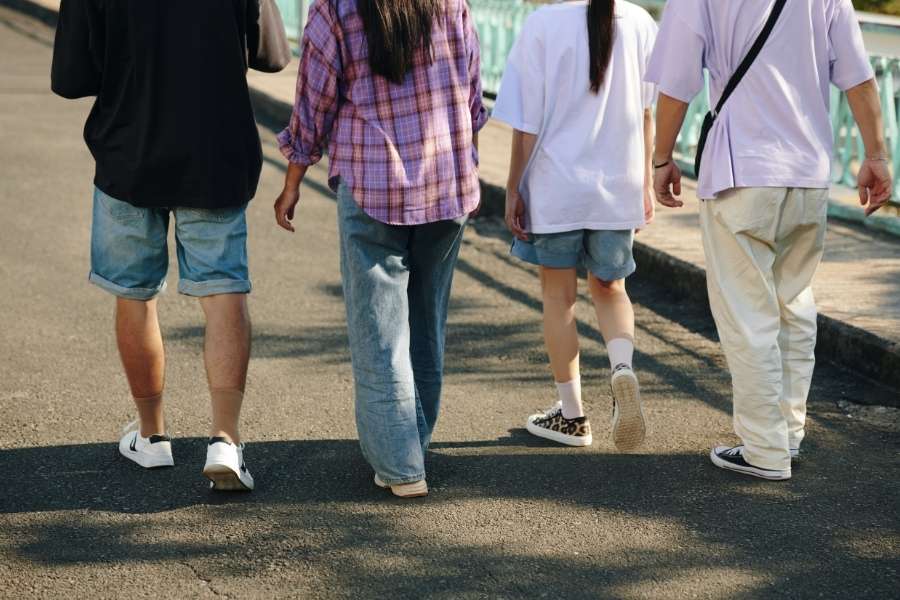 A group of young adults walking away from the camera, showcasing casual, eco-friendly Sustainable Streetwear outfits on a sunny day.