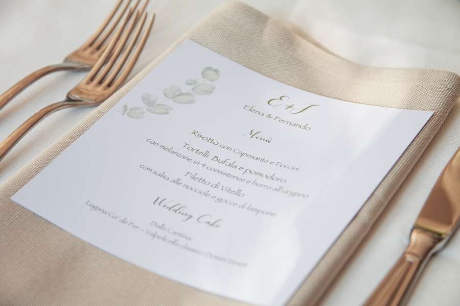 An elegant wedding menu printed on paper and placed on a napkin next to cutlery